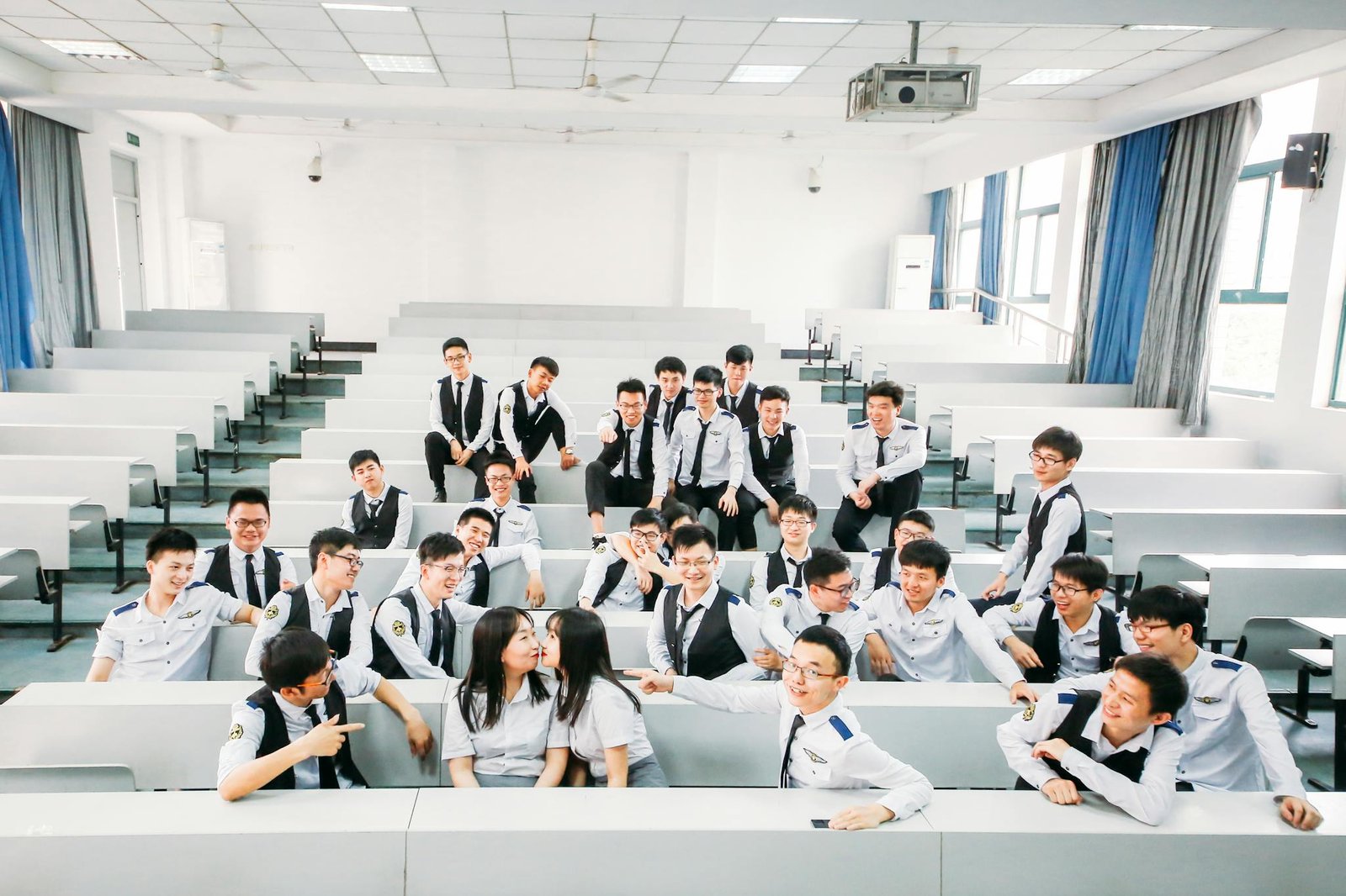 A lively group of college students in uniforms posing playfully in a classroom setting.