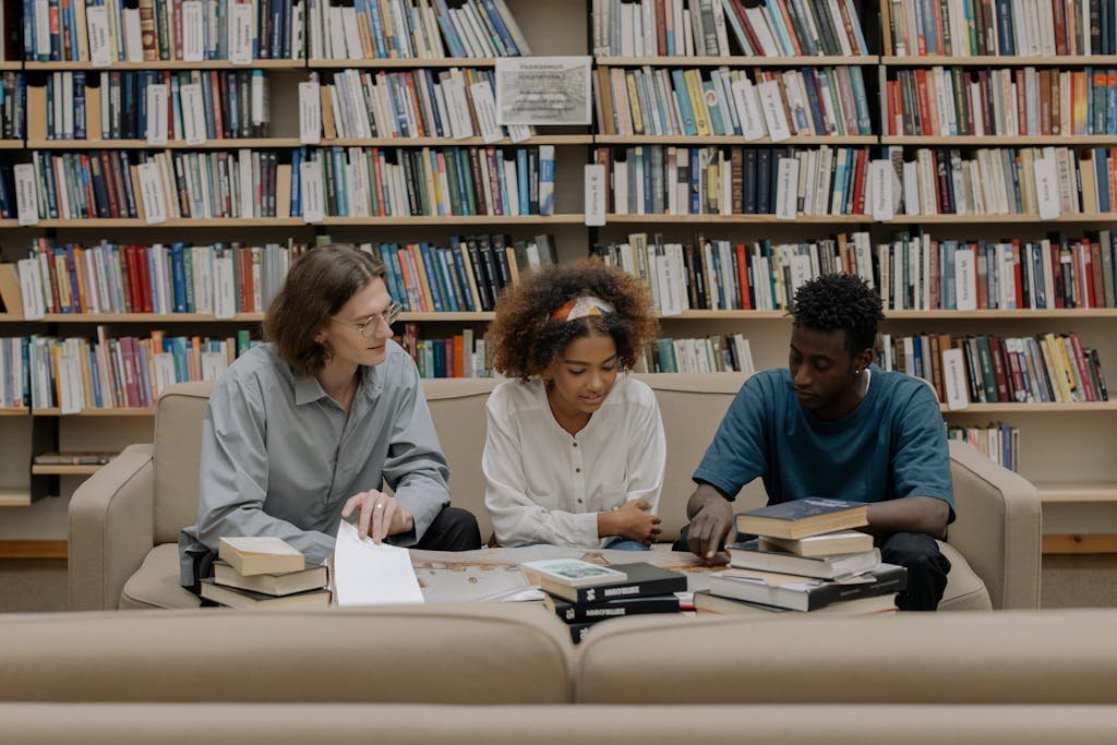 Three students engaged in group study session surrounded by bookshelves.